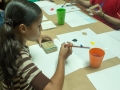 Niña pintando con bloque de madera amarrado con gomitas elásticas